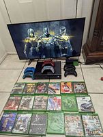 Photo showing Xbox One console, 6 controllers including limited edition redfall and Gears of War 4 red controllers, and 18 Xbox One games arranged on floor in front of 40 inch Sanyo TV.