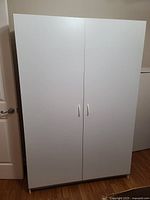 Front view of large white cabinet with two doors and silver handles.