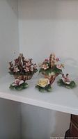 Set of five Capodimonte art glass floral pieces: two floral baskets with handles and three individual flowers on leaf bases, displayed on a white shelf.