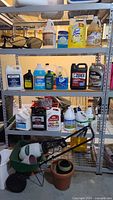 Shelving unit with assorted car fluids including Prestone radiator fluid, Zerex antifreeze, Fram oil, windshield fluids, and household cleaners like Lysol, Simply Green, plus yard seed spreader and weed sprayer, and gardening pots.
