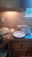 Photo showing a variety of clear glass baking dishes, some with lids, and one white opaque round dish on a kitchen counter.