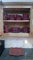 Kitchen cabinet shelf with stacked reddish-brown bowls, plates, cups and bottom counter with a reddish-brown platter.