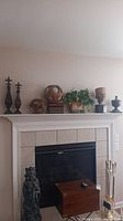 Overall view of mantle with all decorative items arranged on top, showing metal finials, faux books, planter, ceramic head, and rattan balls