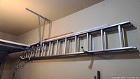 Full side view of the aluminum extension ladder mounted/fixed horizontally on wall, showing length and overall condition
