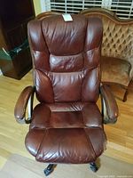 Front view of brown leather style office chair showing padded seat, backrest, and armrests with wear visible on armrests.