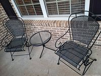Front view of two wrought iron chairs and round glass-top table on porch