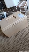 Beige textured plastic sewing box closed, placed on carpet near fireplace