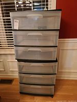 Two Sterlite plastic storage drawer units, each with three drawers and caster wheels, placed on wooden floor against wall with white wainscoting and window blinds.