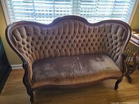 Reproduction Victorian-style tufted velvet settee in front of a window with venetian blinds. The velvet shows variation in light color from brown to mauve hues. Wooden carved frame and curved legs visible. Single armrest repair visible on the right side.
