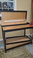 Overall view of work bench showing wooden top and pegboard, with fluorescent light attached.