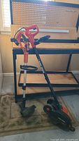 Photo showing two Black and Decker yard tools, an electric edger and a battery-operated weed wacker leaning against a workbench.