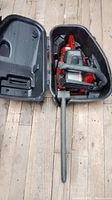 Red and black Snapper chain saw inside black carrying case on wooden floor.