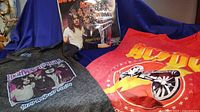 Two sleeveless AC/DC T-shirts and a jigsaw puzzle displayed together on a blue fabric background.
