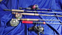 Full view of 4 fishing rods including 2 fly rods with reels and 2 spinning rods with reels on blue fabric background.