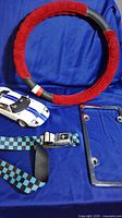 Full lot items on blue fabric background showing Ford GT1 model, belt, steering wheel cover, and license plate holder