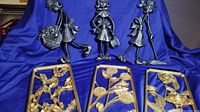 Set of three gold decorative floral wall hangers and three black painted metal golfer figurines on blue background