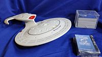 Model of the Star Trek USS Enterprise NCC-1701D with customizable card game materials including deck box containing cards and sealed card booster pack.