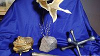 Photo showing gold plated Art Nouveau jewelry box, rock sculpture with brass seagulls, cylindrical container and giant metal jack on blue cloth background.
