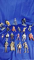 Full lot spread including 18 vintage Star Wars action figures laid out on blue fabric background, showing variety of characters and colors including orange pilot suit, brown cloak, and green headed figure.