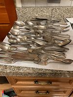 Top-down view of large assortment of silverware showing various forks, spoons, and knives laid out on a countertop.