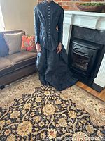 Front view of the antique black wedding dress showing the fitted bodice with multiple buttons, long sleeves, and part of the gathered train on the floor.