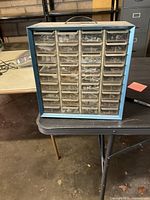 Front view of blue metal storage unit with 36 clear plastic drawers holding assorted hardware items.