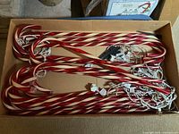 Photo showing bundled red and white striped candy cane yard ornaments with attached white string lights and black pointed stakes, all placed inside a cardboard box.