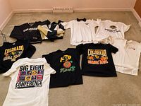 Overview of clothing items laid out on carpet including jackets, sweatshirt, and multiple t-shirts.