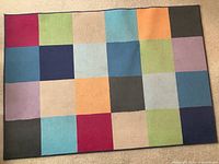 Full view of a rectangular colorful area rug with a grid of 24 squares in various colors including red, green, blue, orange, purple, beige, gray, and black.