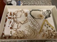 Photo of white and cream beaded necklaces along with a daisy flower pendant and watch-style pendant in a box