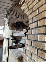 Wooden hanging buffalo-shaped sign with 'GO CU' in black paint, photographed hanging against an exterior brick wall.