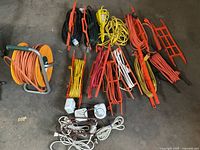 Overview of various extension cords in multiple colors coiled on plastic and metal reels and holders, laid on a concrete floor