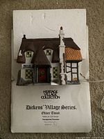 Color photo of the Maylie Cottage handpainted porcelain model on its original white box showing front facade and details including visible 'Maylie Cottage' signs and Heritage Village Collection branding.