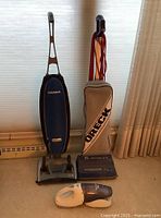 Photo showing two upright Oreck vacuum cleaners side by side with a Black&Decker handheld Dustbuster in front.