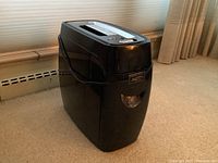 Front angled view of the black Fellowes paper shredder sitting on carpet, showing overall shape and size.