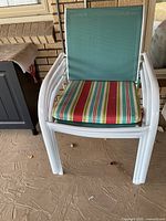 Single white metal frame patio chair with mint green mesh back and multicolor striped seat cushion displayed on concrete floor.