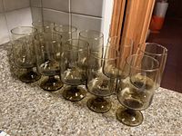 Eight smoky glass drinking cups arranged in two rows on a countertop, showing the uniform size and stemmed base with no visible damage.