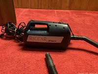 Riccar SupraQuik vacuum cleaner looked in detail with power cord and intake nozzle shown.