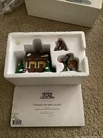 Lot contents in original white foam insert: cabin, woman, man with calf figurines, calf, and paper label with Heritage Village Collection branding.