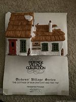 Photo of the handpainted porcelain cottage with brown thatched roof, white walls, chimney, windows and a red door, with a sign reading 'Bob Cratchit & Tiny Tim'.