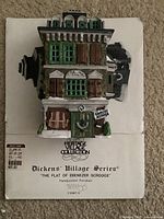 Color photo of the handpainted porcelain building 'The Flat of Ebenezer Scrooge' sitting on its original box showing detailed front facade with green shutters and a wreath on the door.