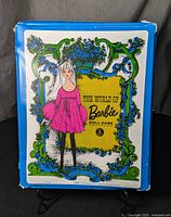 Top view front of case showing colorful Barbie doll illustration with blue floral and green scrollwork border.