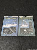 Front view of two Metal Earth 3D model kits featuring Titanic and Black Pearl ships, showing package art and branding.