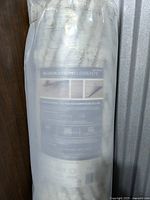Rolled GlucksteinElements Barlow cream and taupe area rug in plastic wrapping showing label with product details.