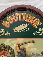 Close-up of top section with the word BOUTIQUE in yellow and red lettering and a golf bag illustration below it