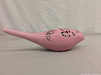 Side angle view of a smooth pink ceramic bird figurine with black Persian calligraphy on top.