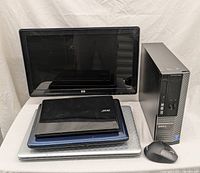 Overview photo showing Dell tower desktop, HP monitor, three laptops stacked (Acer, Toshiba, silver laptop), and a wireless mouse in front