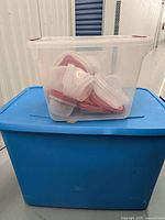Plastic Rubbermaid food storage containers with red lids inside a large clear plastic bin, unevenly stacked.