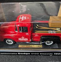 Side and partial top view of the red and black 1957 Dodge D100 Stepside die-cast metal model showing Canadian Tire logos, wooden crates, skis in the truck bed, and the display base label.