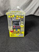 Front view of the Tiny Arcade Pac-Man game in its original sealed packaging showing logo, front arcade cabinet design, and new condition.